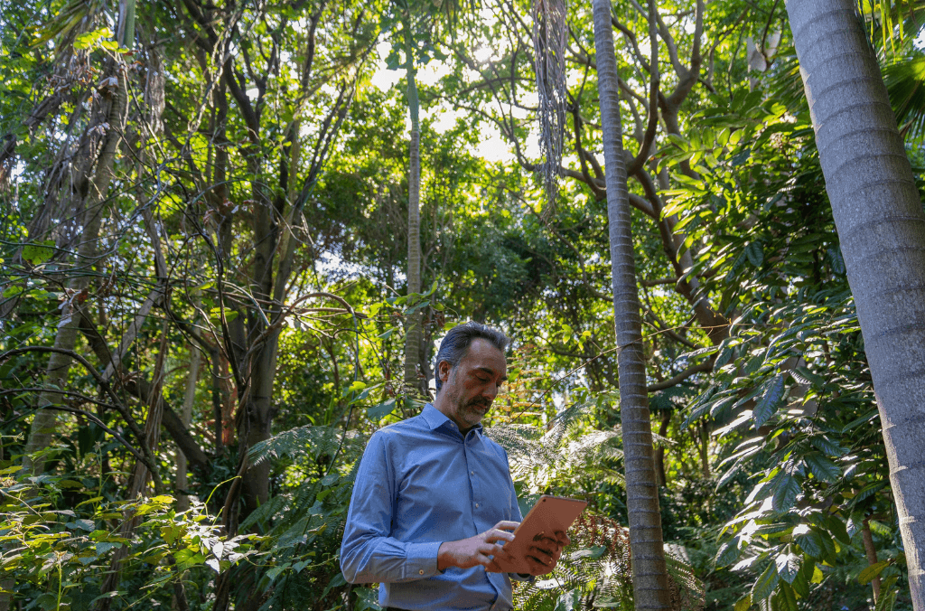A man standing holding an iPad in the rainforest
