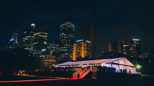 Marquee set up for an event on a lawn at night, with city skyline behind it