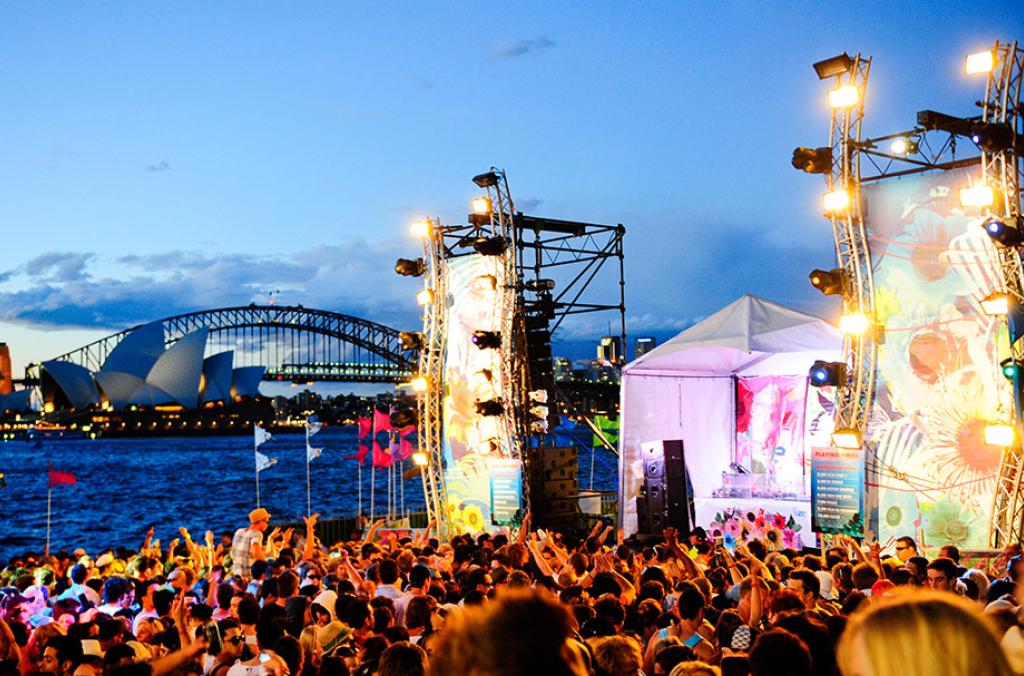 A crowd at a festival and a stage in The Domain with Sydney Harbour in the background